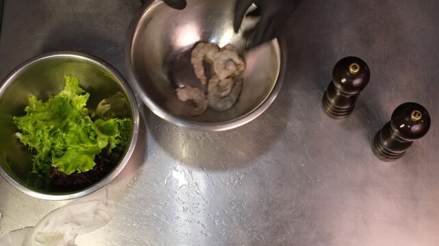 Chefs in gloves marinating raw king prawns before cooking in professional restaurant kitchen top view close-up of hands

