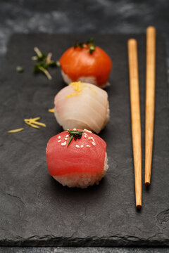 Sushi nigiri set with salmon, tuna and sea bass on black slate plate with chopsticks over dark concrete background. Side view, close up
