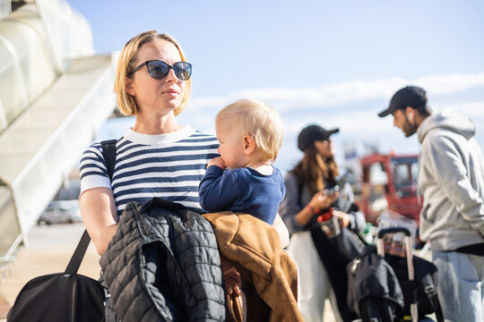 Motherat travelling with his infant baby boy child. Mom holding travel bag and her infant baby boy child while queuing for bus in front of airport terminal station