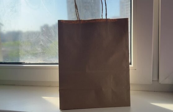 Placing Empty Plastic Bottles into Kraft Paper Bag on Windowsill
A realistic lifestyle video showing empty plastic bottles being placed into a kraft paper bag on a windowsill with a city view 