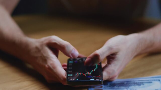 Male trader analyzes crypto exchange on smartphone in investment app. Securities market. Stock chart on screen or display. Man investor holds in hands btc application, cryptocurrency usd