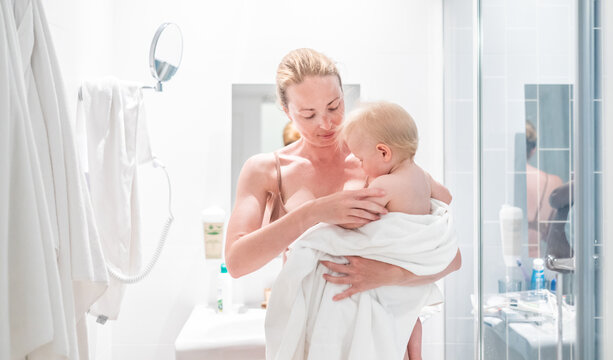 Tender mother holding her baby boy wrapped in a white towel after a bath. Loving connection between a mother and her child in a peaceful moment at home.