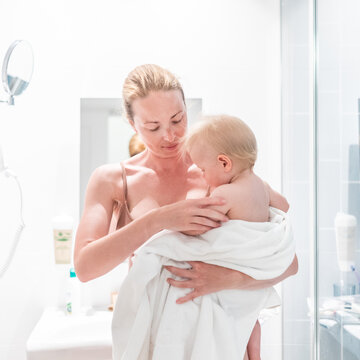 Tender mother holding her baby boy wrapped in a white towel after a bath. Loving connection between a mother and her child in a peaceful moment at home.