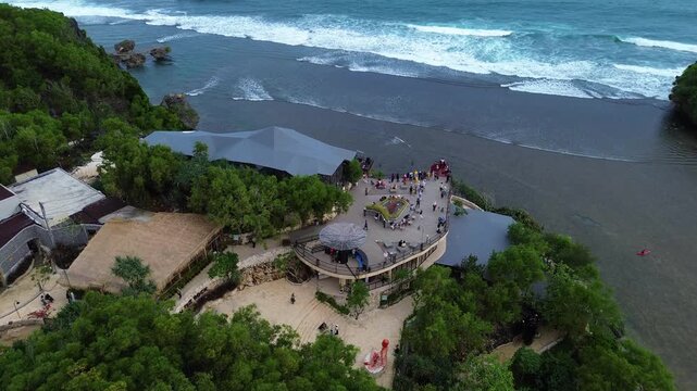 Aerial drone view of Drini Beach in Yogyakarta, Indonesia. Scenic tropical coastline with white sandy beach, clear turquoise water, small offshore island, and gentle ocean waves.
