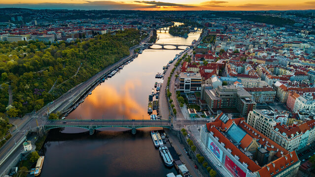 Aerial view of the Vltava River with historic bridges, docked boats, and red-roofed buildings during sunset in Prague, Prague, Czechia.