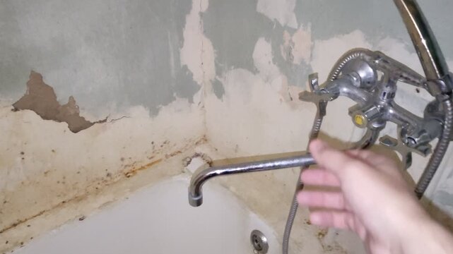 Person turning on water faucet in old peeling bathtub, first person view