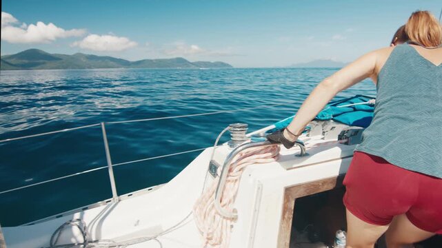 Couple sailing in the tropical calm sea during nice sunny day. Man steers the boat, woman walks and checks the dashboard inside the vessel