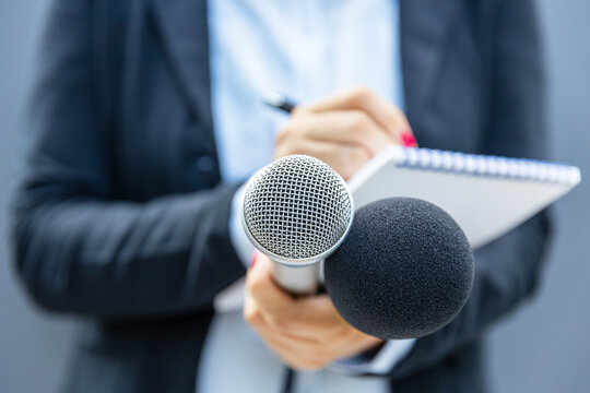 Female journalist holding microphones and taking notes at press conference or media interview event