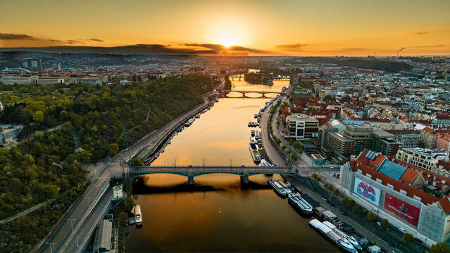 Aerial view of the Vltava River and Cech Bridge at sunset with the city skyline and lush greenery in Prague, Prague, Czechia.