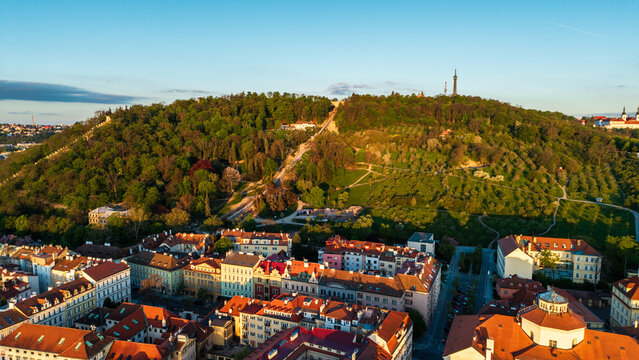 Aerial view of Petrin Hill and the lookout tower overlooking historic red-roofed buildings and lush greenery during golden hour in Prague, Prague, Czechia.