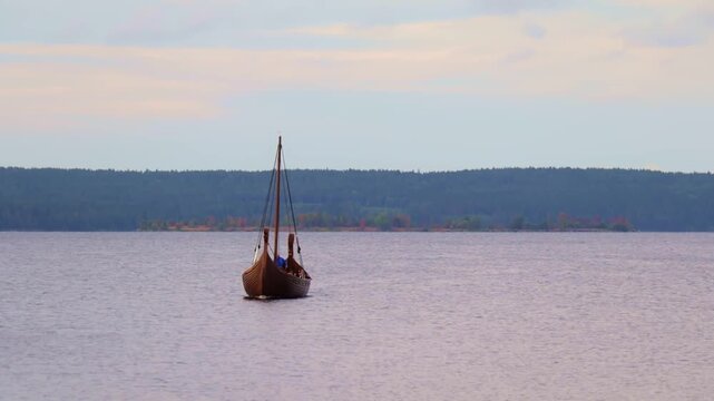 Solitary traditional longship sails smoothly over the tranquil lake surface, with a dense forested shoreline forming a dramatic backdrop. The soft light and still water create a serene, almost mythica