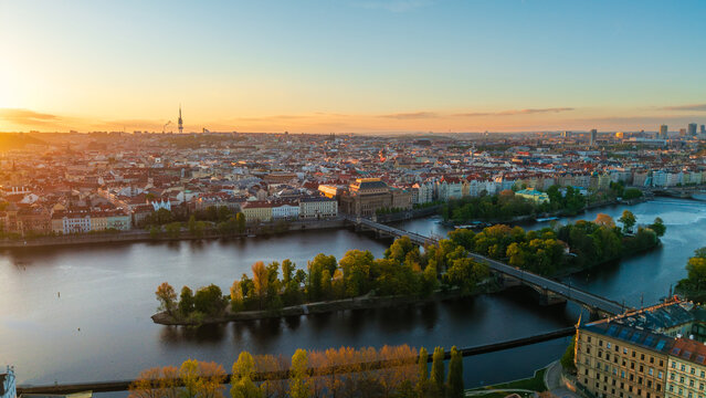 Aerial view of the Vltava River and the historic skyline during sunset with bridges, lush green islands and the Zizkov Television Tower in Prague, Prague, Czechia.