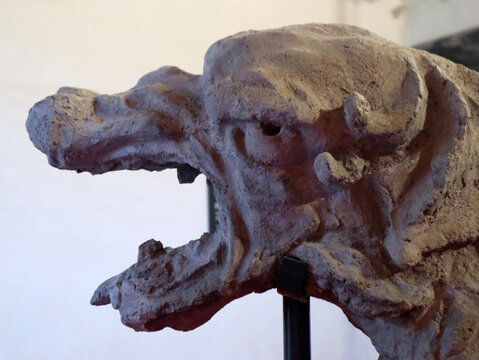 Primo piano di un antico gargoyle in pietra raffigurante una creatura mostruosa con le fauci spalancate in un interno storico