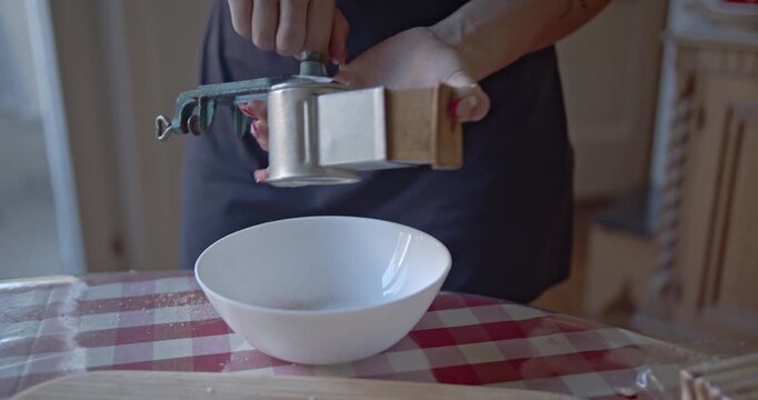 A woman prepares ingredients in her kitchen, meticulously grating dry biscuits into a white bowl to create fine crumbs for a homemade recipe or baking project.