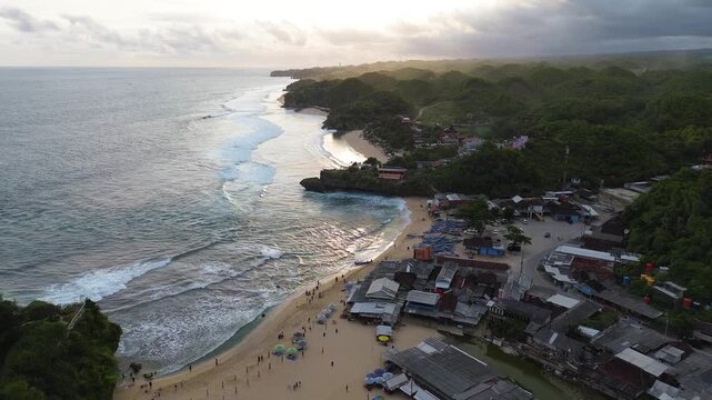 Aerial drone view of Drini Beach in Yogyakarta, Indonesia. Scenic tropical coastline with white sandy beach, clear turquoise water, small offshore island, and gentle ocean waves.