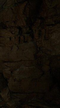 The scene shows the inside of a cave with rough stone walls. Shadows fill the space, creating a dark environment. The cave appears natural with no signs of human presence.