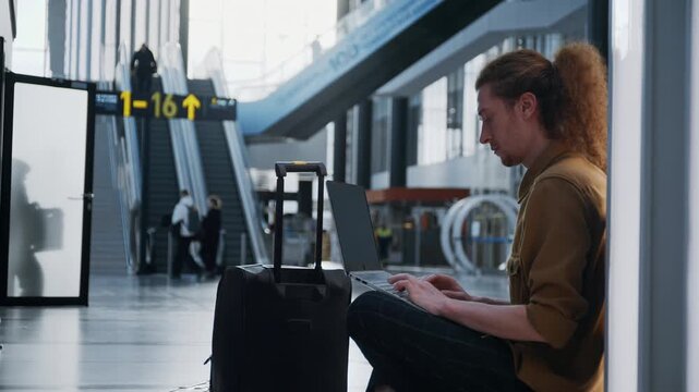 Casual man working remotely on a computer while waiting for his flight at the airport terminal