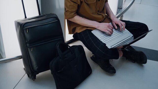 Freelancer sitting on the floor of an airport departure lounge and working on a laptop