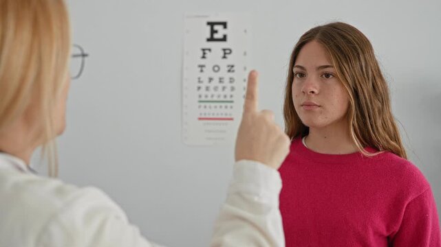 Woman patient smiles while optician points finger at eye chart in clinic; health reassurance vision care.