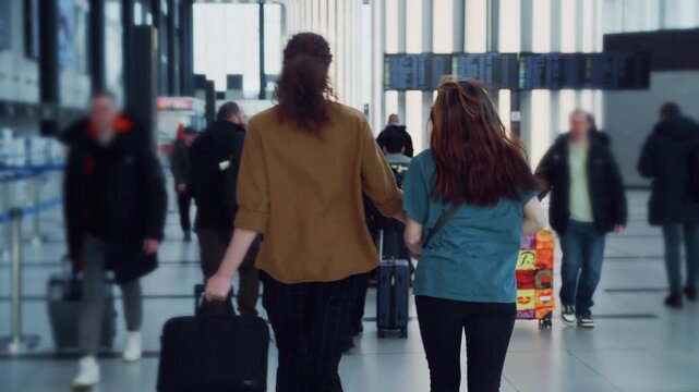 A couple races through a bustling airport terminal, checking the gate information on screens as they run.