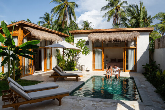 Couple sitting at the edge of a swimming pool enjoying their private tropical villa