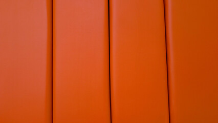 Orange leather upholstery paneling creating a modern geometric background texture with vertical stripes, showcasing abstract patterned padding and material details © Newleks