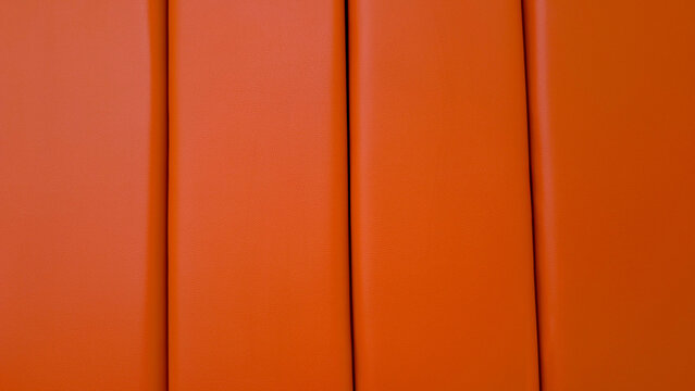 Orange leather upholstery paneling creating a modern geometric background texture with vertical stripes, showcasing abstract patterned padding and material details