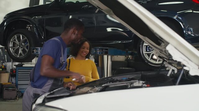 Male auto mechanic using an open-end spanner hand tool during car service and talking with a female customer in the repair garage.