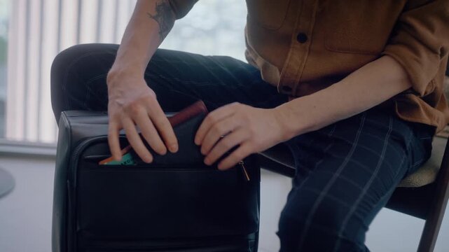 A traveler reaches into the front compartment of his rolling carry-on bag, pulling out his boarding pass and identification