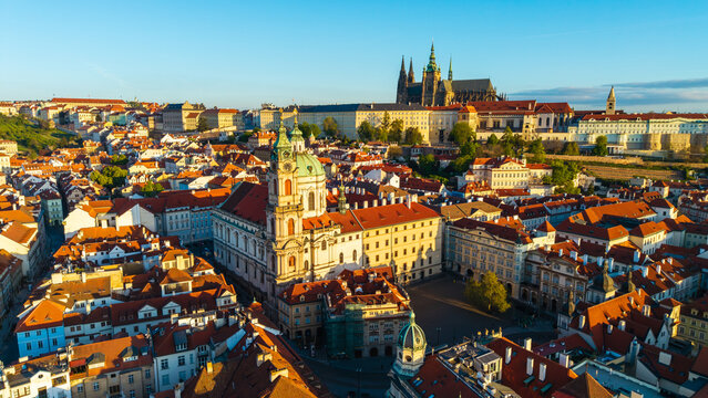 Aerial view of St. Nicholas Church and Prague Castle overlooking the historic red rooftops of the Lesser Town under a clear blue sky during golden hour in Prague, Prague, Czechia.