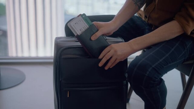 Unrecognizable male passenger placing travel documents into the front pocket of his carry-on suitcase