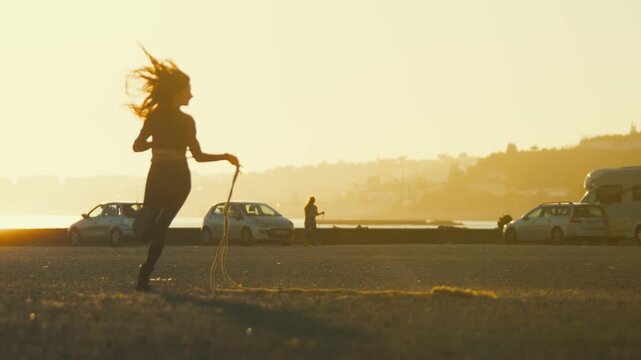 Jump rope session takes place on the beach at sunset with a young woman enjoying the warm evening light