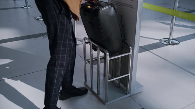 Male passenger placing a suitcase into a sizing gauge to check baggage dimensions at the airport