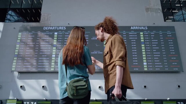 Young man and woman looking at the flight information display at the airport before their trip