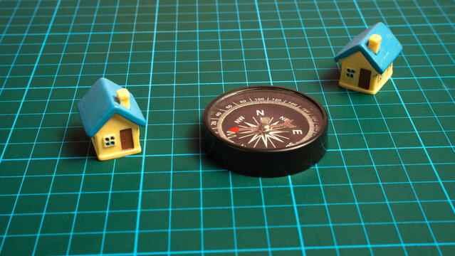 Black magnetic compass positioned between two miniature toy houses representing real estate search and direction