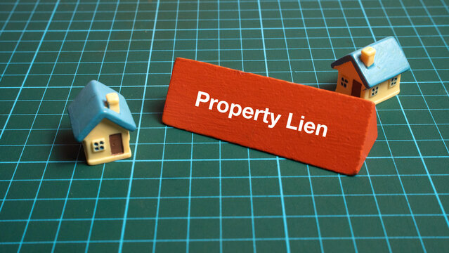 Property Lien red sign placed between two miniature toy houses on green grid background for real estate legal concepts