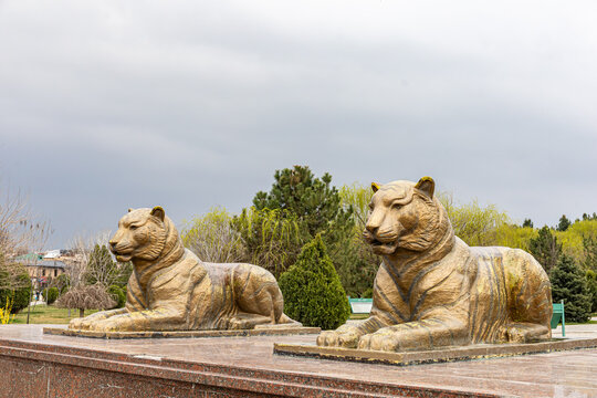 Guardian tigers, side profile of golden tiger statues on a raised granite platform in Amir Temur park, Samarkand.