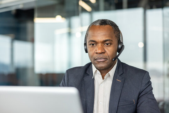 Male customer service agent in a suit jacket and shirt, wearing a headset and working intently on a laptop in a modern office, providing focused remote client support and communication