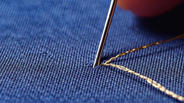 Closeup of a needle and golden thread stitching blue denim fabric.