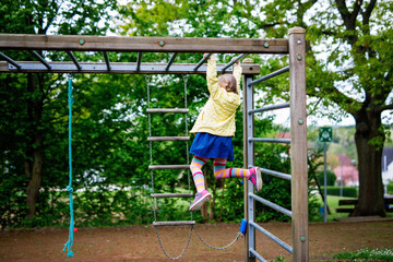 Fototapeta premium Little girl doing gymnastics on a climbing frame, horizontal bar on school yard. Child enjoying school break.