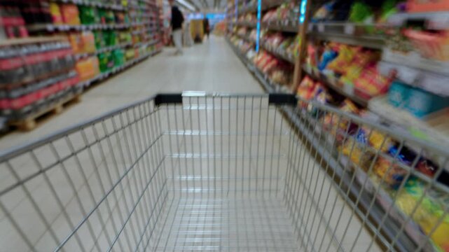 Timelapse from a shopping cart in family hypermarket, fast moving through supermarket aisle. Food store, grocery shop. POV customer trolley moving into mall. Shelves of products. Immersive experience