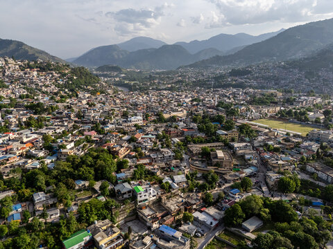 Aerial view of the dense urban landscape and residential buildings nestled within a green valley surrounded by the Himalayan mountains Muzaffarabad, Azad Kashmir, Pakistan.