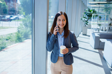 Fototapeta premium Smiling businesswoman talking on phone holding coffee cup