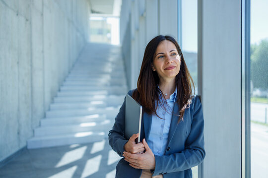 Businesswoman holding laptop looking away in modern office