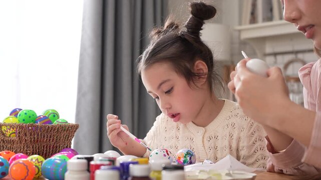 Asian mother and little daughter painting colorful easter eggs with brush at kitchen, Happy family spring holiday celebration, childhood creative art craft learning, motherhood childcare, easter day