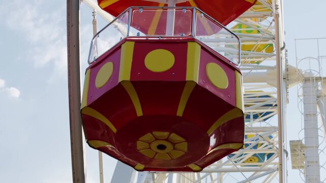 Brightly colored cabin of a Ferris wheel hovers against a clear sky, its bold red and yellow design catching the eye. The scene conveys a sense of playful excitement and leisure, evoking memories of f