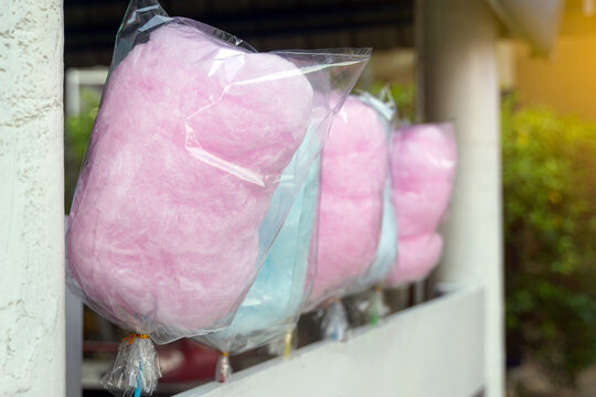 Sweet pink and blue cotton candy wrapped in clear plastic bags hanging for sale. This vibrant candy floss evokes a sense of childhood nostalgia, carnival atmosphere, and festive street food.