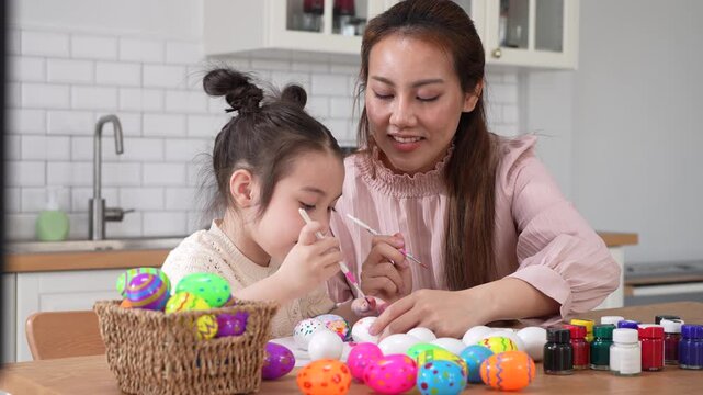 Asian mother and little daughter painting colorful easter eggs with brush at kitchen, Happy family spring holiday celebration, childhood creative art craft learning, motherhood childcare, easter day