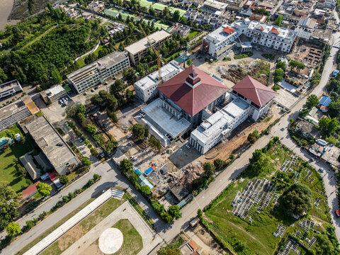 Aerial view of a large institutional building with a red roof surrounded by urban development, lush green trees, and a construction site in Muzaffarabad, Azad Kashmir, Pakistan.