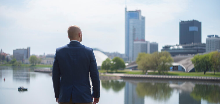 Successful businessman looking at city skyscrapers skyline dreaming of future opportunities with copy space